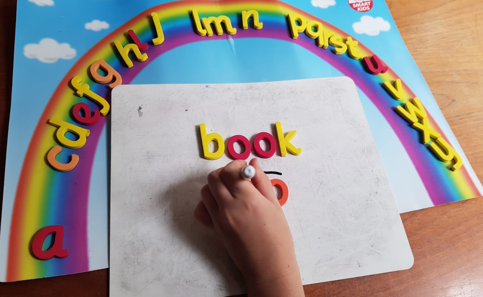 A child building the word 'book' with magnetic letters under a rainbow alphabet arc